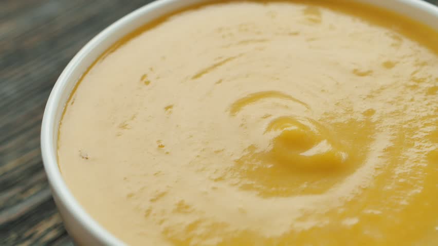 Close-up view of green uk pouring into pumpkin soup in a white plate