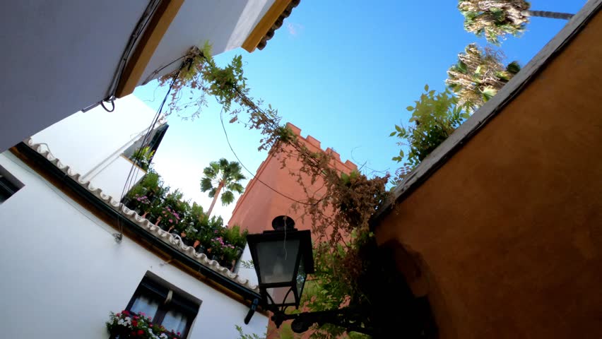 TILT SLOW MOTION SHOT - Royal Palace of Seville Tower (Real Alcazar), old house and lamp at Seville Juderia barrio in Andalusia, Spain.