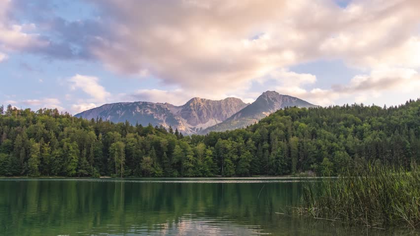 Sunset time lapse of mountain lake Alatsee. Wild nature and pine forest. Fast clouds movement.