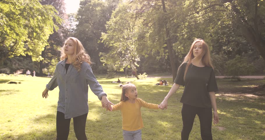 Two young mothers are walking in the park with daughter