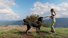Girl plays with stick with dog-Rottweiler on cliff of mountain in valley of Rhodope Mountains