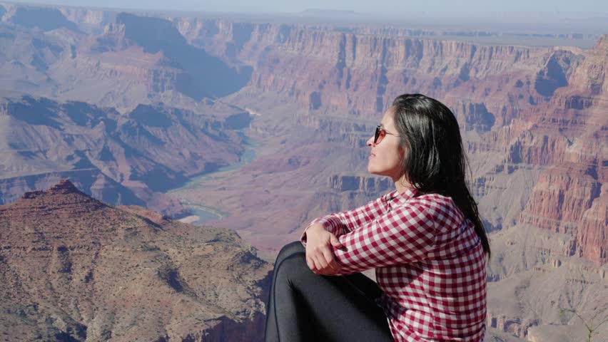 Grand Canyon, Arizona -  tourist woman, sitting on a rock contemplating Grand Canyon scenic view
