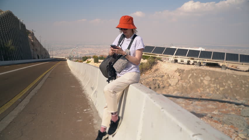 Young auto woman stops on road outdoors spbas. Beautiful Caucasian female sits by roadside and looks with smile, tries to stop cars and spends time in countryside. One pretty person is waiting for
