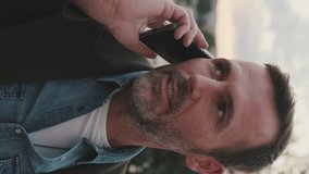 VERTICAL VIDEO: Close up, man talking on mobile phone while standing on the embankment of the river