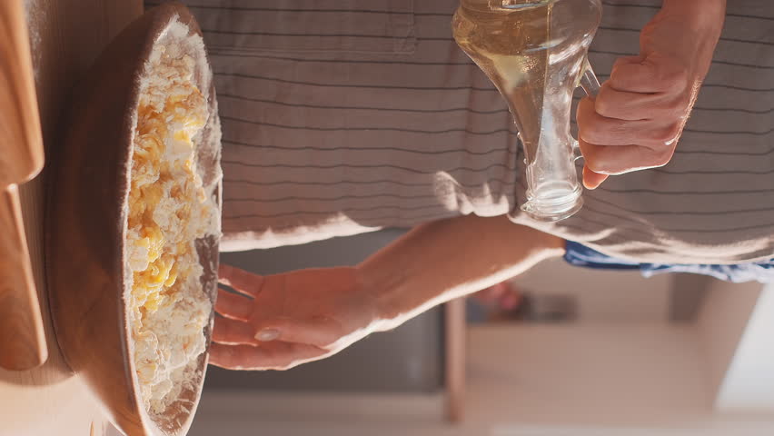 Closeup vertical shot of a woman pouring olive oil into a bowl to make pasta dough according to traditional recipe. A woman cooking at home, enjoying hobby Royalty-Free Stock Footage #1101223523