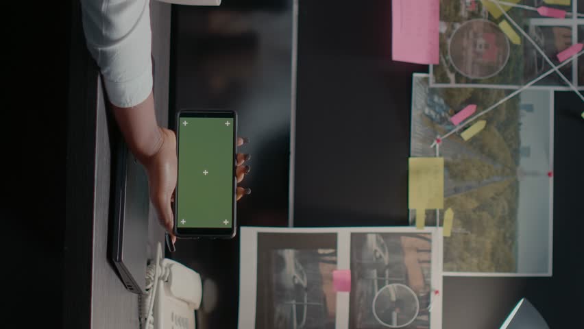 Vertical video: Young inspector using greenscreen in archive office space, examining chroma key display and conducting investigation. Detective checking isolated mockup template with copyspace. | Shutterstock HD Video #1101228493