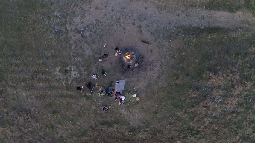 Friends enjoy campfire together on clearing off path aerial top down rising