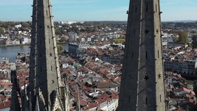 Drone flying around gothic spiers of Bayonne Cathedral with cityscape, France. Aerial orbiting