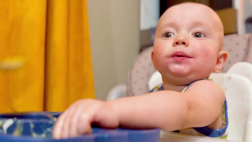 mom feeds baby at the table. dirty a baby newborn dirty mouth eats from spoon. happy family kindergarten proper nutrition newborn. baby lifestyle eats fruit puree from a spoon