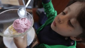 One little boy eating strawberry ice cream on bowl sitting at restaurant table. Child eats sweet dessert with spoon - Powered by Shutterstock - Get 15% off with code: PIKWIZARD15