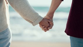 Video of close up of beautiful couple holding hands while walking in a cold winter on the beach.