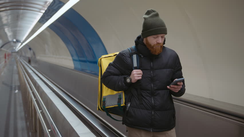 Portrait of a male courier who looks at the delivery address while riding an escalator in the subway