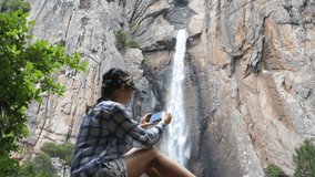 Young woman uses a smartphone to video a beautiful view with waterfall, Corsica, Piscia di Ghjaddu