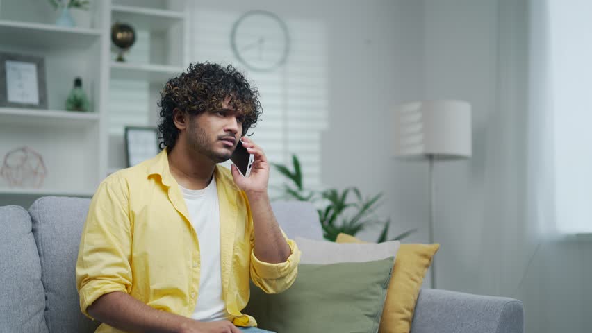 Angry evil young adult man arguing and complaining about bad service talking on the phone while sitting on the sofa at home quarrel with the smartphone Unhappy latin male customer screaming indoor  Royalty-Free Stock Footage #1101262123