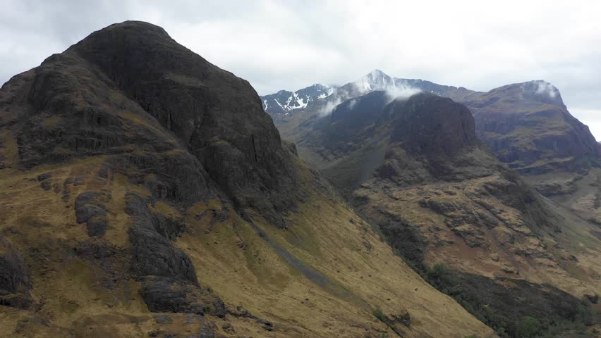 Aerial view of highlands in Scotland, with clouds over the famous mountains known as Three Sisters of Glencoe - Moody weather in Scottish highlands - Background ready image of beautiful landscape