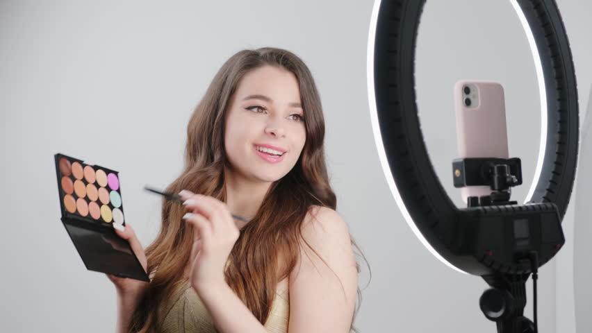 Beautician records video for followers on smartphone showing makeup process. Woman shows shadow palette to paint blush with brush closeup Royalty-Free Stock Footage #1101267277