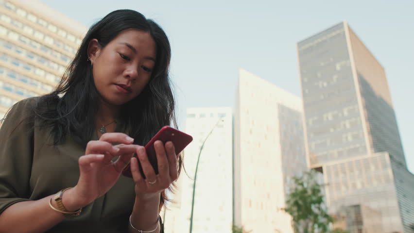 Young girl uses smartphone while sitting on modern buildings background | Shutterstock HD Video #1101272623