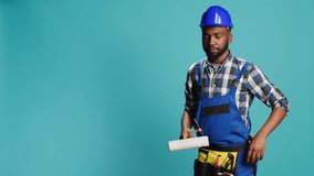 Repairman in overalls painting walls with roller brush, using renovation equipment on camera. Confident carpenter with helmet working with rolling paint brush to change color in studio. - Powered by Shutterstock - Get 15% off with code: PIKWIZARD15