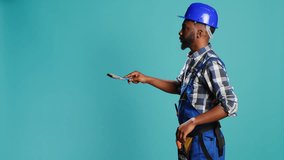Young carpenter painting walls with paintbrush on camera, using renovating tools to change color. Professional craftsman working with brush on reconstruction equipment on blue backdrop. - Powered by Shutterstock - Get 15% off with code: PIKWIZARD15