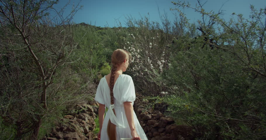 Woman running in park with cherry flowering trees in slow motion. Girl in white dress with long hair in garden. Slim lady moving fast outdoors.