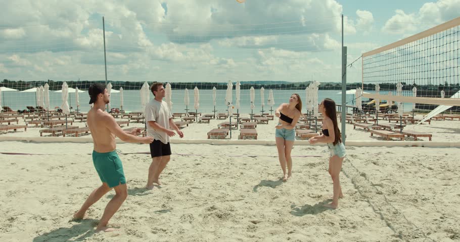 Group of young joyful friends playing volleyball on the sandy beach