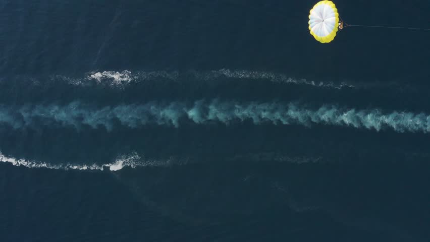Aerial view of a person doing parasail with a motorboat along the coast in Sicily, Italy.