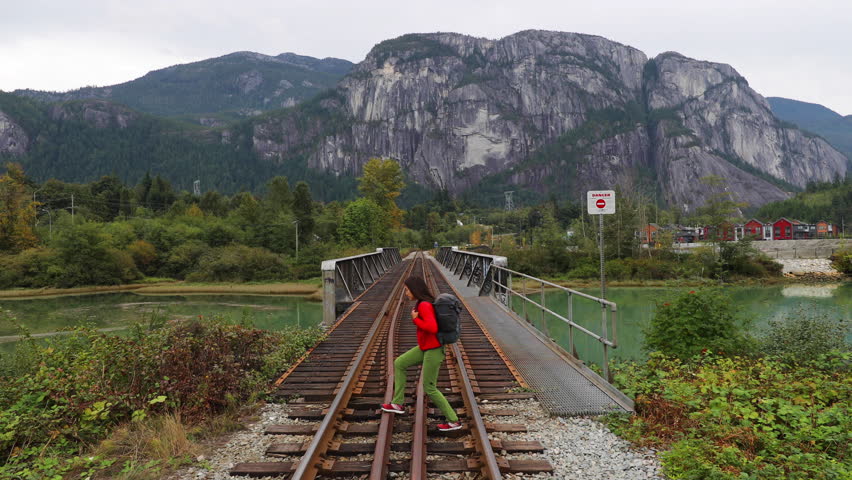 Hiking, backpacking and travel concept video with person walking on railway in iconic nature landcape in Squamish with Stawamus Chief Mountain in background. Woman traveler in British Columbia, Canada