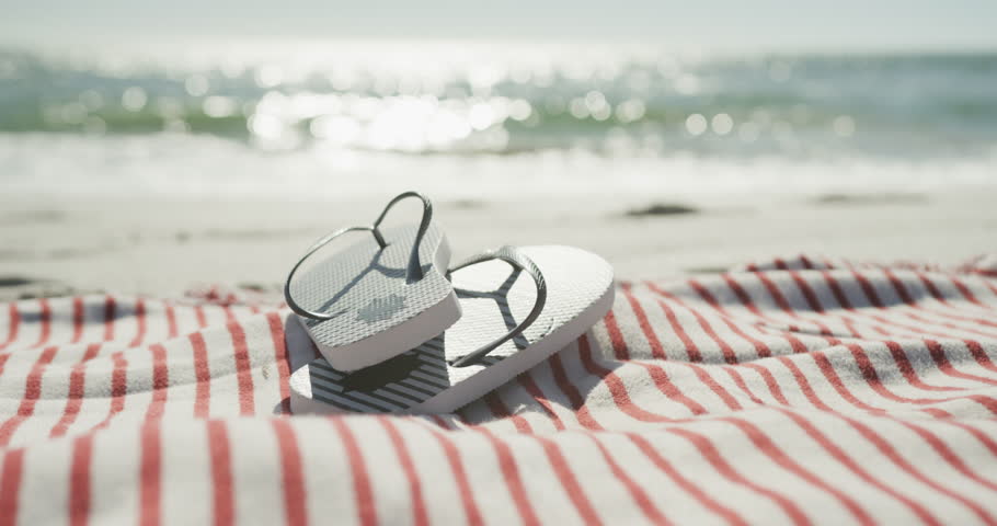Close up of flip flops and towel on beach, in slow motion, with copy space. Summertime, lifestyle and vacation concept. Royalty-Free Stock Footage #1101293803