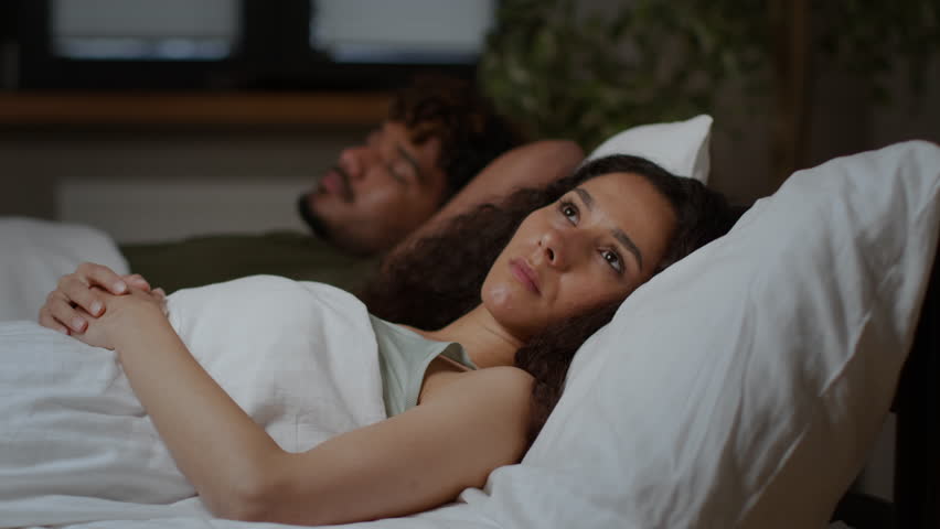 Insomnia concept. Young middle eastern woman suffering from sleep disorder, lying near her sleeping husband in bed with open eyes and thinking about her life, tracking shot, free space Royalty-Free Stock Footage #1101297719