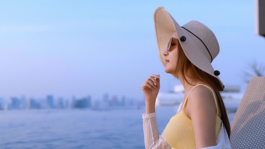 smiling cheerful asian adult woman in bikini relax casual sun bathing on pool bench rooftop swimming pool urban city lifestyle,summer vacation travel ,woman sit on bench happiness peaceful carefree 