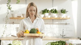 A beautiful blonde bought a lot of vegetables and fruits, a vegetarian is happy in her kitchen, because there are a lot of vegetables and fruits on the table for cooking healthy food.
