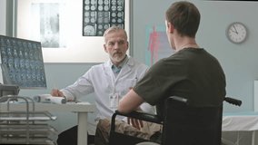 Young Caucasian soldier in wheelchair visiting medical doctor for checkup appointment, looking at MRI scan on computer monitor and having conversation - Powered by Shutterstock - Get 15% off with code: PIKWIZARD15