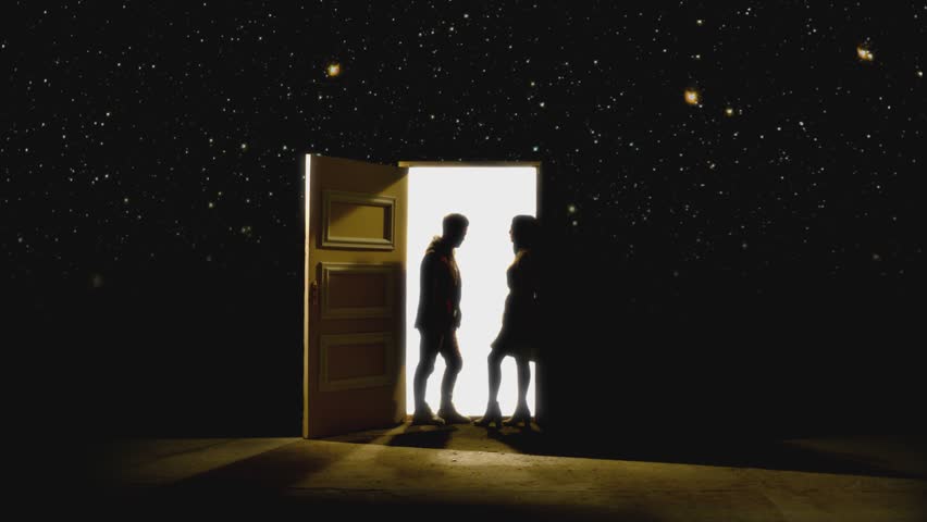 Side view of couple standing opposite and looking each other in front of an open door with white light behind . Footage of couple stand on floor behind stars.  Concept of dream or romance. Slow Motion