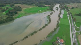 AERIAL: Greatly increased river water level flooding farm lands by the riverside. Muddy flood water spilling over river banks after heavy rainfall in autumn and covering grassland, fields and forest.