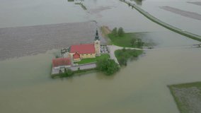 AERIAL: Village church and cemetery are surrounded by flooded agricultural land. Incredible view of inaccessible church in the middle of muddy floodwater. Heavy rainfall caused flooding in countryside