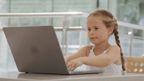 Close-up view of little girl using laptop while studying remotely. Portrait of cute, caucasian girl typing a keyboard while studying outdoors. High quality 4k footage