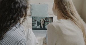 Happy young women making online video call using laptop talking showing thumbs-up waving hand in bedroom at home. Millennials and communication concept.