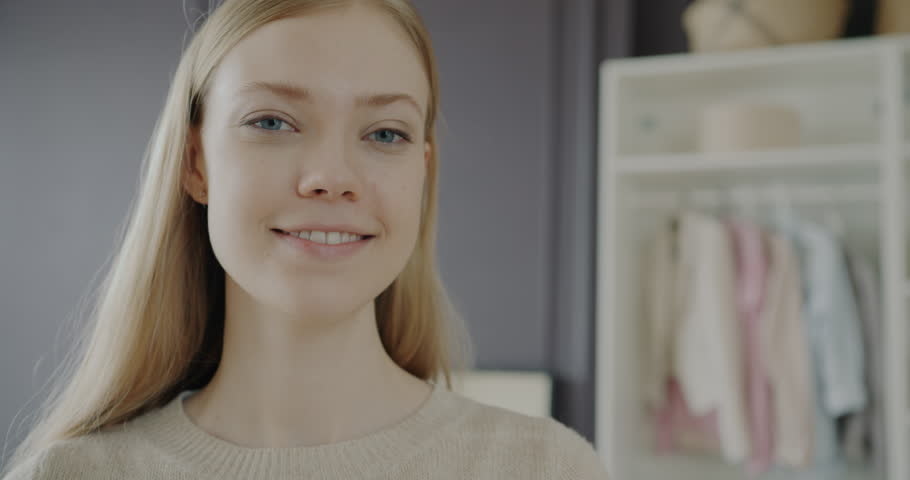 Close-up portrait of joyful lady with blond hair standing at home with wardrobe full of clothes in background. People and fashion concept.