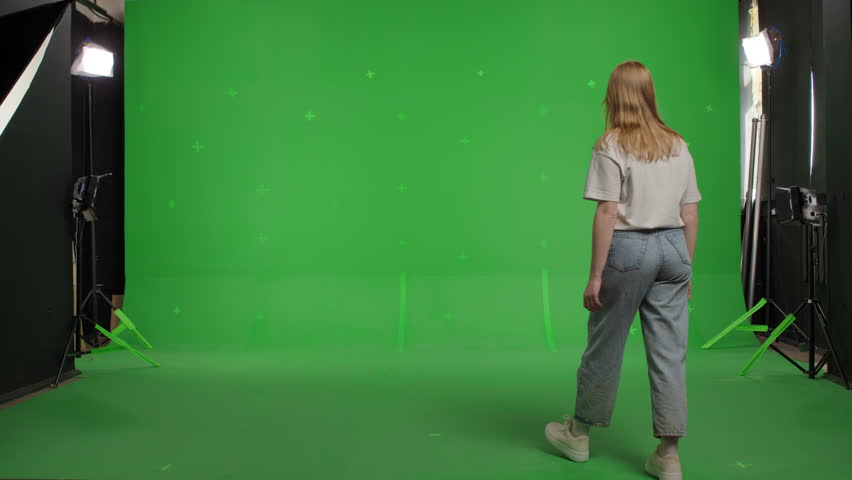 red-haired attractive white race young woman in jeans and a white T-shirt walks with her back to the camera on a green background. The girl turns around and gets scared Royalty-Free Stock Footage #1101309775