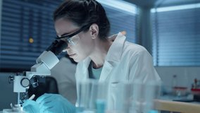Female scientist in sterile gloves, protective glasses and white coat using microscope and taking notes while doing research in laboratory - Powered by Shutterstock - Get 15% off with code: PIKWIZARD15