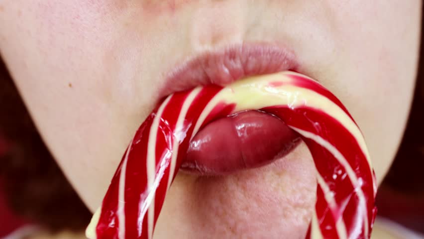 Young woman licking sweet Christmas red and white candy cane stick close up