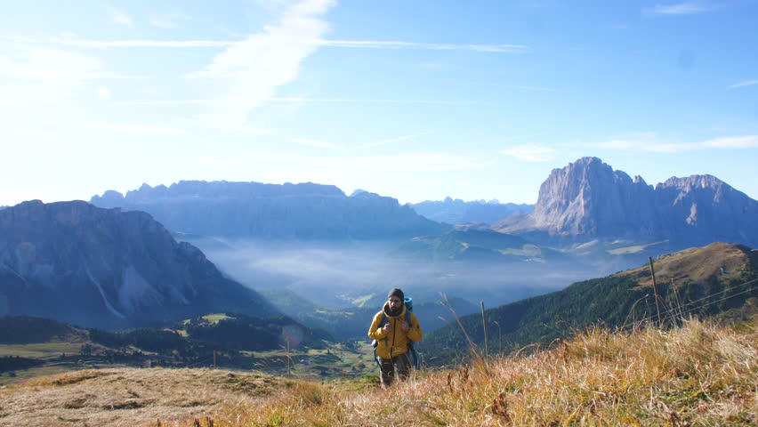 Young man hiking at Seceda mountain arriving to peak at sunrise. Backpack, yellow jacket, boots, beanie. Traveling to puez Odle, Dolomites, Trentino, Italy. Royalty-Free Stock Footage #1101319111