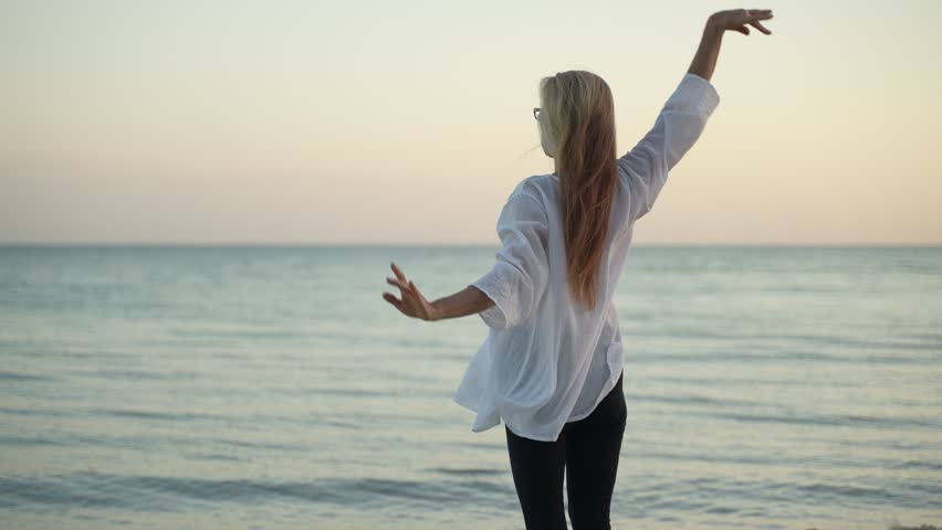 Fit slim mature senior woman stretching practicing yoga and dancing during the morning sunrise on the beach.