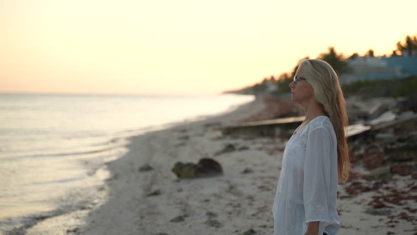 Fit slim mature senior woman stretching practicing yoga and dancing during the morning sunrise on the beach.