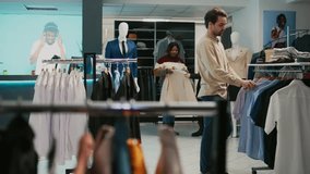 Male store assistant helping client to buy shirts at mall, diverse people talking about new fashion brands. Customer and employee examining formal or casual wear, shopping center.