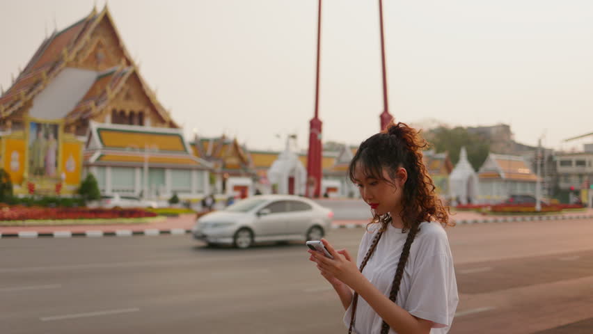 Happy of A young Asian traveler uses her mobile phone or smartphone to capture and share her experience of the Giant Swing, an iconic landmark of Bangkok, on social media
