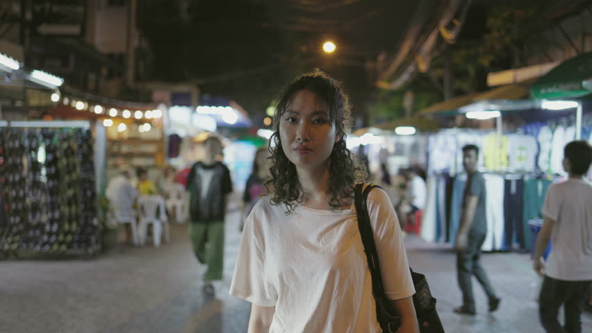 Young female traveler smiling and posing for the camera in the vibrant and bustling Khaosan Road at nighttime in Bangkok, Thailand.