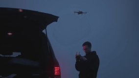 A young guy takes a photo or video with a drone. The pilot controls the copter in the evening or at night. Travel blogger by car by nature. Adventures of a lonely man. Road trip