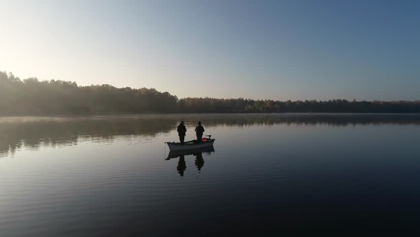Aerial silhouette view of two anglers on a fishing boat it the middle of the lake. Two fishermen fishing at sunrise.