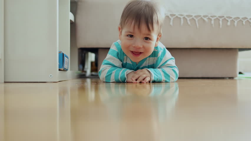 Toddler exploring home. Little baby boy with happy face crawling on the floor and smiling.